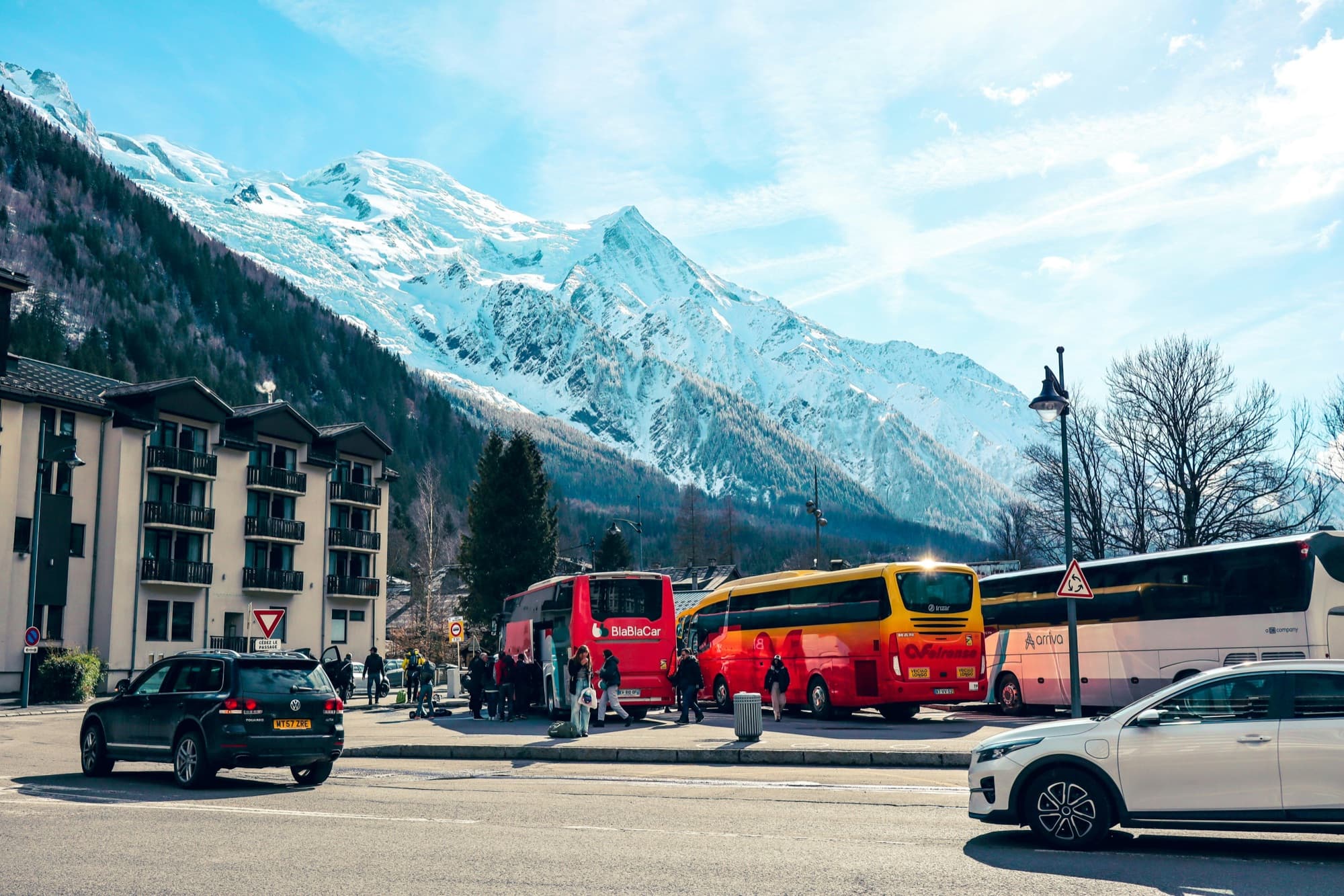 Mehrere Reisebusse stehen in einem Alpenort vor verschneiten Bergen