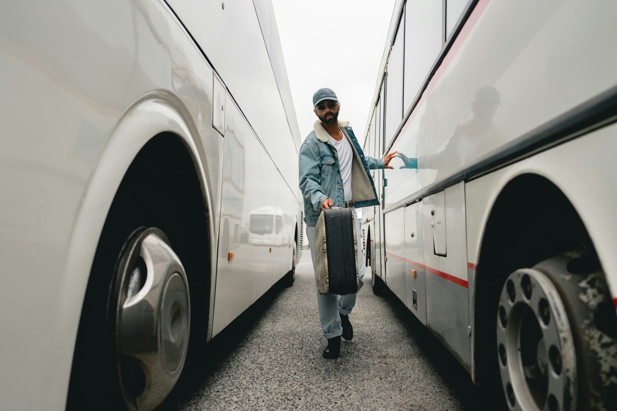Ein Reisender mit Koffer geht zwischen zwei abgestellten Reisebussen hindurch