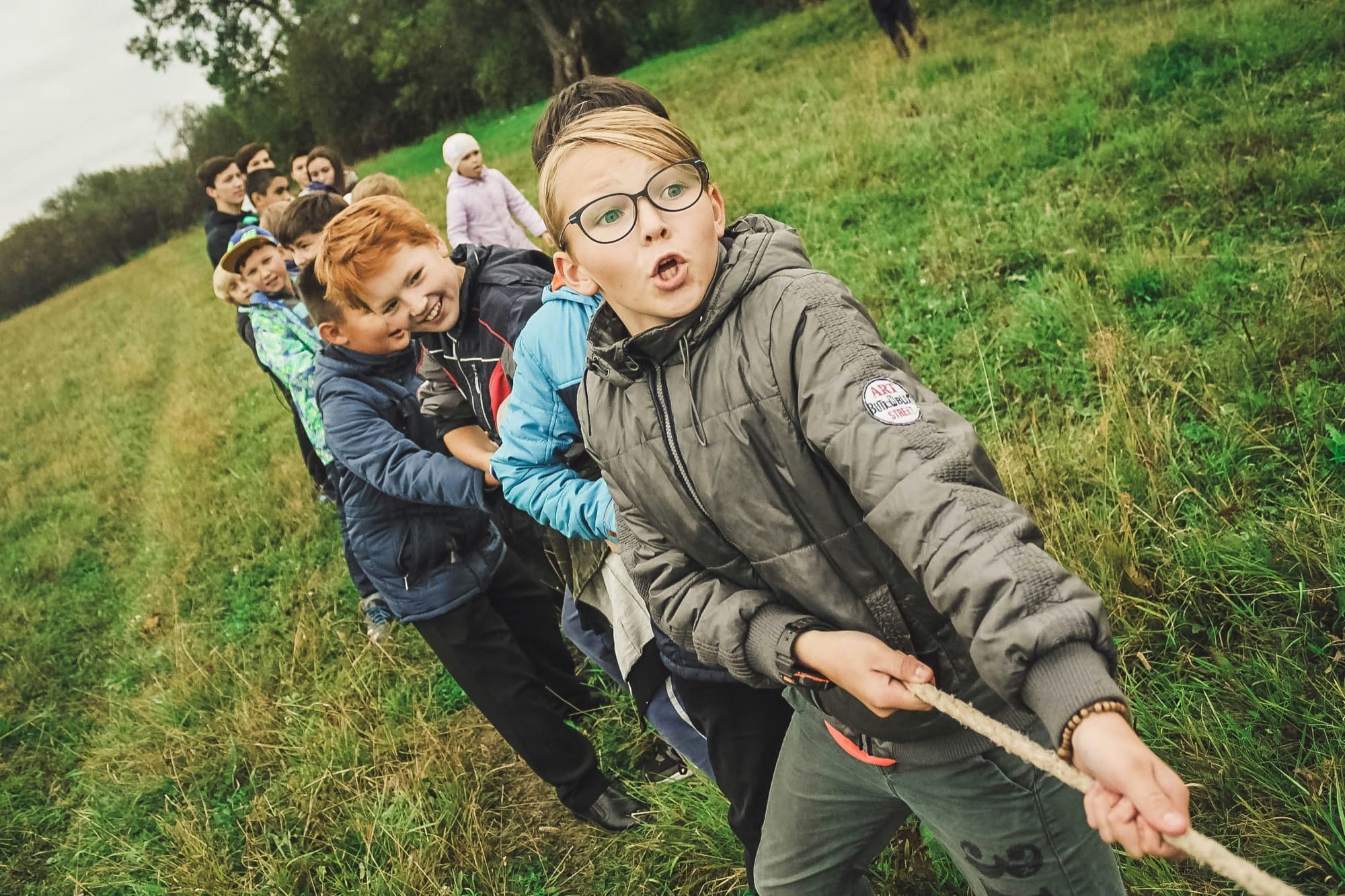 Kinder ziehen bei einem Spiel gemeinsam an einem Seil über eine Wiese