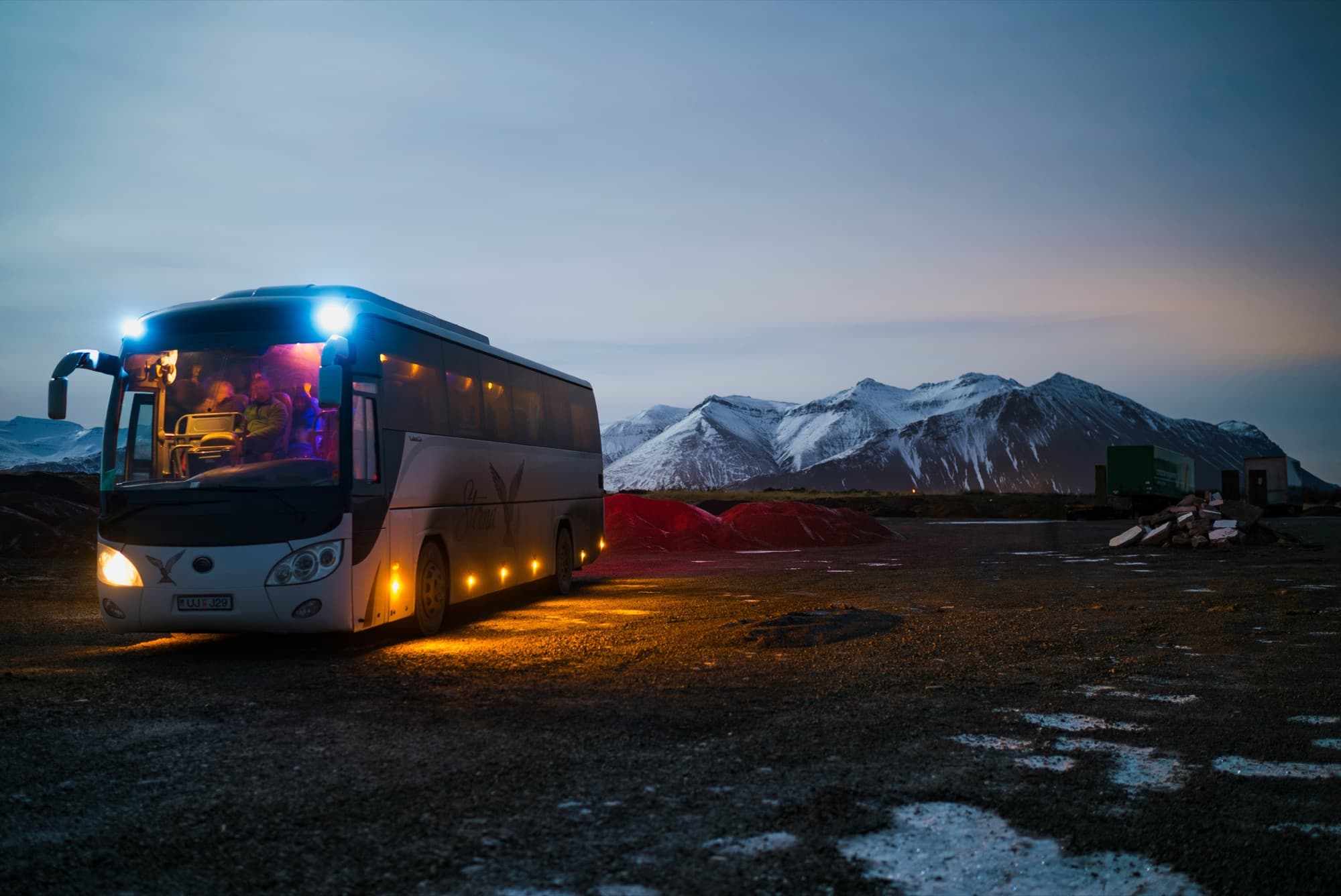 Reisebus mit eingeschalteter Beleuchtung in der Dämmerung vor einer Bergkette